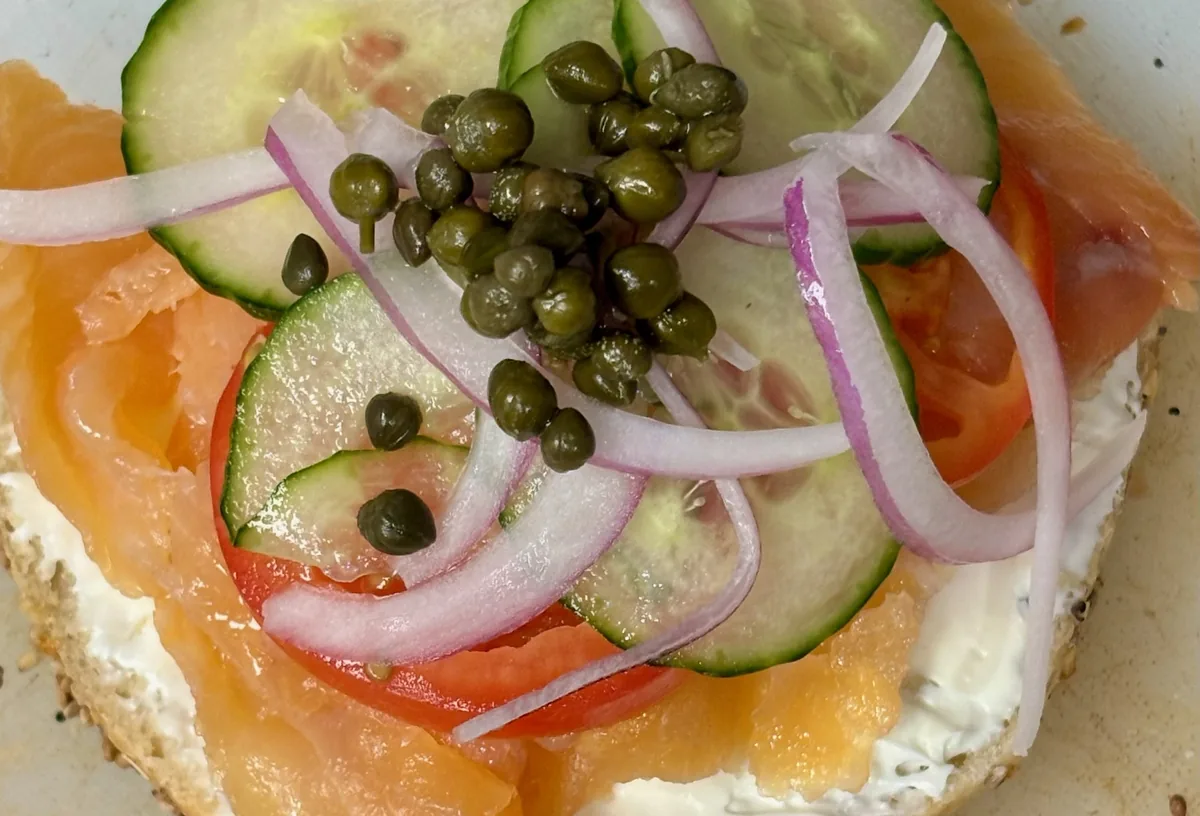 An open-faced lox bagel with cream cheese, tomato, cucumber, red onion and capers