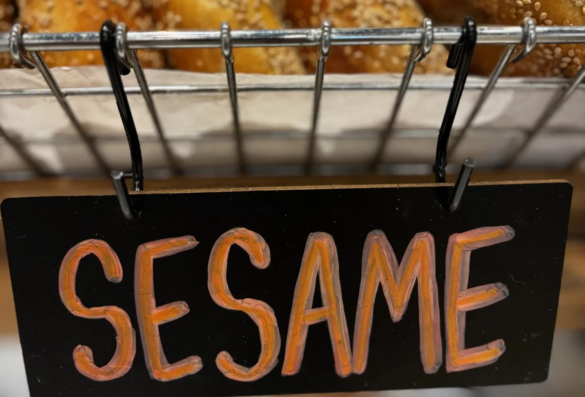 A hand-lettered sesame sign hanging under a basket of fresh sesame bagels at B's Bagels